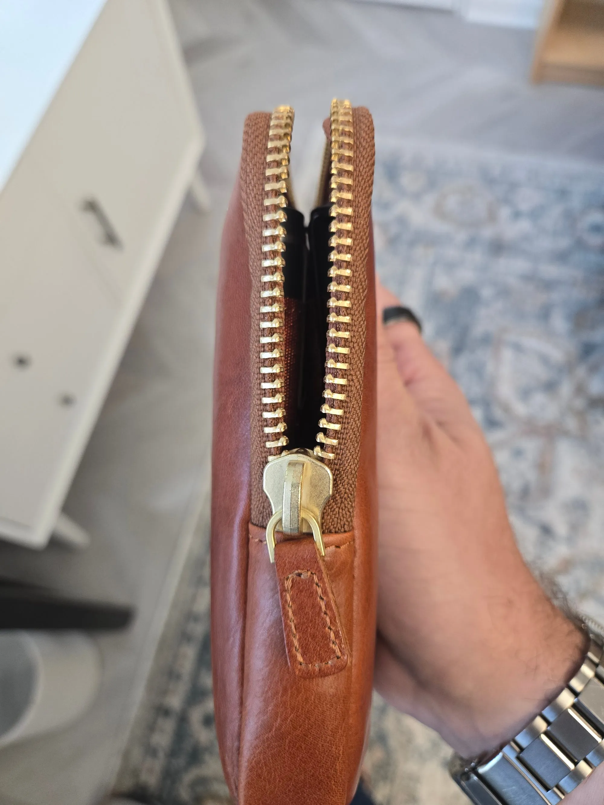 A close-up of the pen case's brass-colored zipper running along the edge of the cognac leather.